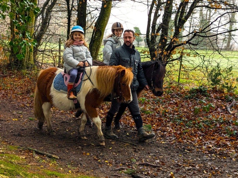 Enfant en balade à poney en main au Brévedent, accompagnée d’un adulte dans les sous-bois.